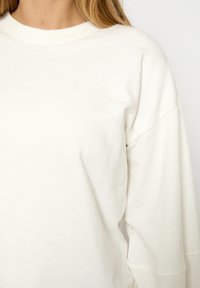 Lichtbeige sweatshirt gemaakt van zacht katoen. Heeft lange mouwen, een ronde halslijn en een losse pasvorm met minimale stikdetails.