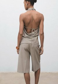 Haut halter beige avec un dos dénudé et un détail noué, associé à un short beige ample. Comprend un tatouage dans le dos et un bracelet épais.