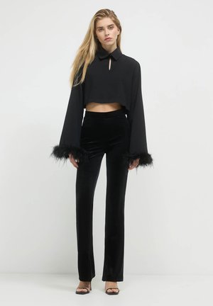 Black crop top with a collar and keyhole detail, paired with black velvet pants. Top features feather accents on the sleeves.