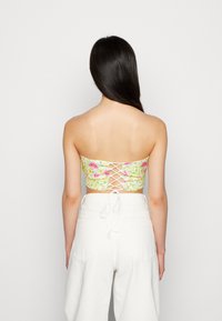 Top bandeau floral com padrões amarelos, rosas e verdes. Apresenta um detalhe de costas com laço. Usado com calças brancas de cintura alta.