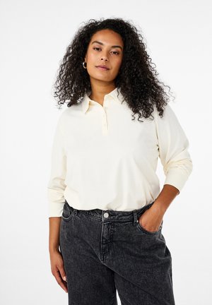 Cremfarbener Langarm-Polo-Shirt mit einem geknöpften Kragen, kombiniert mit hochtaillierten, dunkelgrauen Jeans. Glatte Stofftextur, lockere Passform.