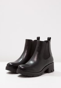Czarne skórzane botki za kostkę z elastycznymi panelami po bokach, okrągłym noskiem i masywną podeszwą z teksturowanym bieżnikiem dla lepszej przyczepności.