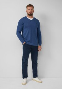 Blauer, gestrickter Langarm-V-Ausschnitt-Pullover, kombiniert mit dunkelblauen Hosen und weißen Sneakers. Glatte Textur mit subtilen Logo-Details.