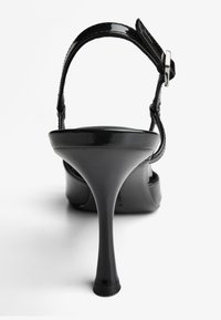 Čierna dámska sandála na vysokom podpätku s lesklým povrchom, tenkým remienkom okolo členka a zužujúcim sa podpätkom, s hladkou polstrovanou stielkou.