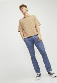 Beżowa polówka z prążkowanego materiału, z krótkimi rękawami, w połączeniu z niebieskimi spodniami typu slim-fit i ciemnymi sneakersami. Strój ma luźny krój i gładką teksturę.