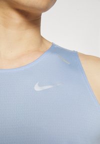 Light blue athletic tank top made from textured fabric, featuring a round neckline and Nike logo in white on the chest.