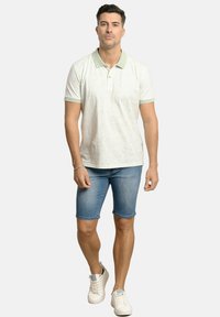 Camiseta polo verde claro con textura estampada, mangas cortas y cuello a juego, combinada con pantalones cortos de denim azul y zapatillas blancas.