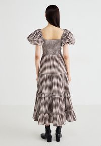 Bruine en witte geblokte maxi-jurk met pofmouwen, geribbelde lijfje, gelaagde rok en een vierkante achterkant. Zwarte kniehoge laarzen.