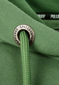 Tessuto di felpa verde con maglia testurizzata. Occhiello argentato con incisione "SPITZBUB" che tiene un cordoncino intrecciato verde.