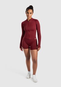 Bordeaux atletisk sæt med en langærmet top med fuld lynlås og højtaljede shorts, lavet af strækbart stof, med et tætsiddende design.