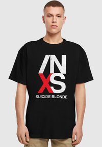 Sort bomulds t-shirt med fede hvide og røde grafiske bogstaver "INXS" samt teksten "SUICIDE BLONDE" i et moderne skrifttype. Korte ærmer.