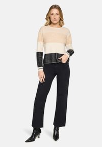 Sweter dzianinowy w poziome paski w kolorach beżu, kremu i czerni. Posiada długie rękawy i prążkowane wykończenia. Połączony z czarnymi spodniami o szerokich nogawkach.