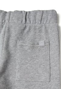 Šedé tepláky s měkkou texturou, elastickým pasem a náprsní kapsou s malou logovou značkou na zadní straně.