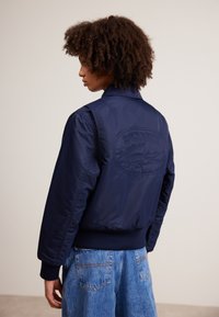 Námornícka bombrová bunda s rebrovanými manžetami a lemom, s reliéfny logom Lacoste na chrbte, vyrobená z hladkého, ľahkého materiálu.