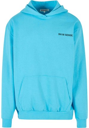 Gaiši zilas krāsas kapuce no mīksta auduma, ar priekšējo kabatu, ribinātiem piedurkņu galiem un mazu teksta logotipu uz krūškurvja.