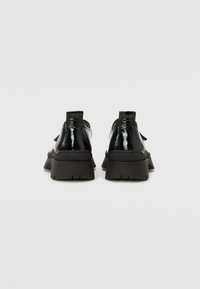 Μαύρα παππούτσια από πατεέν με χοντρή μαύρη σόλα, που διαθέτουν λεία επιφάνεια και λαβή στο πίσω μέρος για εύκολη φόρεση.