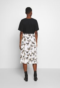 Zwart shirt met korte mouwen gecombineerd met een witte rok met een meerkleurig vogelpatroon, elastische tailleband en zichtbare zwarte enkellaarsjes.