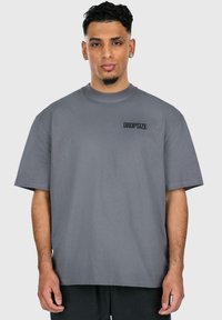 Grå bomulds t-shirt med korte ærmer, der har en rund halsudskæring og en sort "DROPSIZE" print på venstre brystområde.