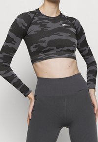 Zwarte en grijze camouflage lange mouwen crop top met een getailleerd ontwerp; gecombineerd met hoog-wijde grijze leggings met ribbelaccenten.
