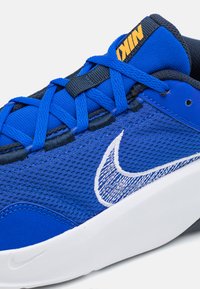 Blå joggesko med mesh-overdel, teksturert stoff, hvit Nike-logo og gummisåle. Inkluderer blå snøringer og en polstret krave.