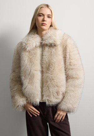 Beige Fake-Fur-Jacke mit hohem Kragen, Reißverschluss und flauschiger Textur. Verfügt über voluminöse Ärmel und einen kurzen Schnitt.