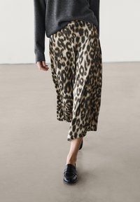 Spódnica midi w zwierzęcy nadruk w kolorze leopardzim z satynowego materiału, o swobodnym kroju z szerokim dołem, w połączeniu z czarnymi loafersami i ciemnym swetrem.