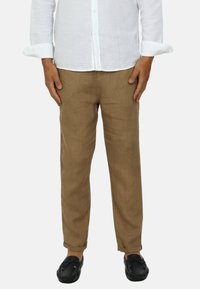 Pantaloni di lino marrone chiaro con vestibilità rilassata, con orli arrotolati e tasche laterali, abbinati a scarpe slip-on nere.