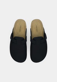 Ζευγάρι μαύρων σανδαλιών με λουράκια που κλείνουν με αγκράφα και μπεζ εσωτερικές σόλες με το λογότυπο "Pier One", εκτεθειμένα σε λευκό φόντο.