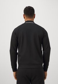 Svart sweatshirt med långa ärmar, ribbade ärmslut och rundad halsringning. Har en slät textur och en slim fit design.