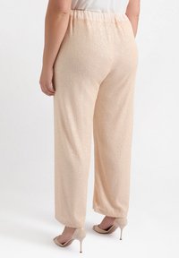 Pantaloni a gamba larga color pesco pallido con strisce verticali testurizzate e paillettes. Presentano una vita elastica e un tessuto morbido e leggero.