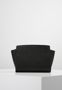 Černá kabelka s pevnou konstrukcí, vyrobená z hladké kůže, obdélníkového tvaru, se šikmými stranami a minimalistickým stylem bez viditelného kovového příslušenství.