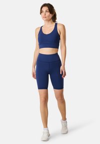 Completo sportivo blu navy composto da reggiseno e pantaloni corti realizzati in tessuto elastico. Il reggiseno presenta spalline larghe; i pantaloni corti hanno una lunghezza fino a metà coscia con una vita alta.