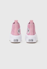 Różowe, płócienne sneakersy wysokie mają białą gumową podeszwę, kontrastową czarną naszywkę z logo oraz pętelkę z tyłu, ułatwiającą zakładanie.