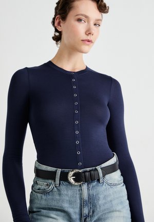 Tumesinise pika varrukaga bodysuit ümmarguse kaelusega, millel on ees nuppudega kinnitamine ja kerge kangas. Sobivad kõrge vöökohaga denim lühikesed püksid ja must vöö.