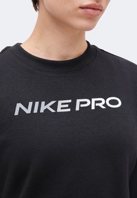 Gros plan d'une personne portant un t-shirt noir avec un texte blanc "NIKE PRO" sur la poitrine, montrant le cou et le bas du visage.