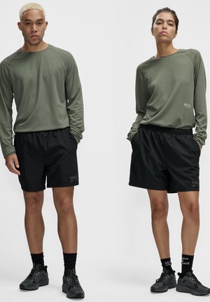 Sorte træningsshorts med elastisk talje, parret med en langærmet olivengrøn top med struktureret stof og lille logo-detalje.