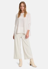 Pull léger blanc à manches larges, associé à un pantalon large crème. Le modèle porte des bottines beige. Texture lisse, coupe décontractée.