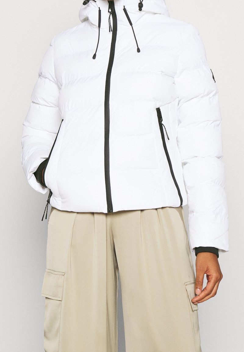 Hvid dunjakke med hætte, sort lynlåslukning og snoretræk. Har sidelommer og et let cropped design. Glat tekstur.