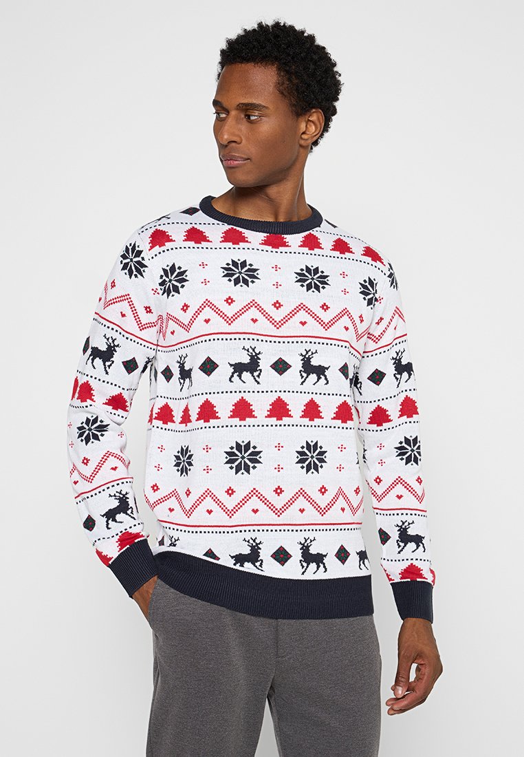 Biały sweter z dzianiny z czerwonymi i czarnymi wzorami bożonarodzeniowymi, w tym renifery, drzewa i płatki śniegu, z granatowym, prążkowanym dekoltem.