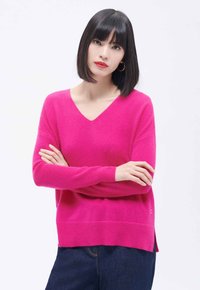Sweter z dekoltem w serek, z długim rękawem w jasnoróżowym kolorze, wykonany z miękkiego materiału. Lekko luźny krój z bocznymi rozcięciami oraz ściągaczami przy mankietach i u dołu.