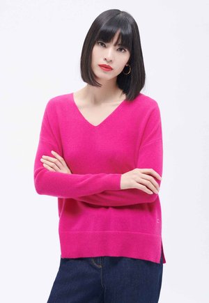 Maglione a V, maniche lunghe, di un vivace colore rosa, realizzato in tessuto morbido. Vestibilità leggermente ampia con spacchi laterali e polsini e bordo a coste.