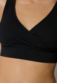 Svart ruggad bralette med en insvept design och en bred ände nedtill. Har en V-ringning och en slät textur.