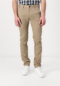 Kharma slim-fit-housut, jotka on valmistettu puuvillasekoitteesta, varustettu nappisulkimella, sivutaskuilla ja sileällä pinnalla, yhdistetty valkoisiin tenniskenkiin.