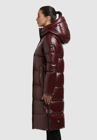 Bordó, fényes kivitelű pehelykabát, kapucnival és cipzáras oldalrésszel. Ujján logóval ellátott felvarró, hosszú, bélelt sziluett.