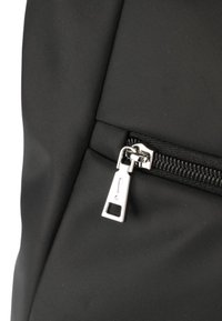 Mochila de tela negra con una cremallera plateada y un tirador rectangular, superficie texturizada y cierre de cremallera seguro.