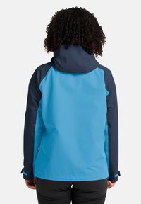 Veste imperméable avec un corps bleu clair et des manches et des accents bleu marine. Comprend une capuche réglable et des poignets élastiques.