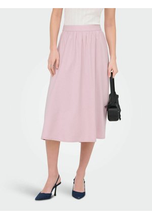 Kobieta ubrana w jasnoróżową midi spódnicę z wysokim stanem, granatowe szpilki na obcasie z paseczkiem na pięcie, trzymająca małą czarną torebkę, stojąca na białym tle.