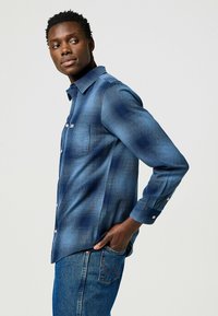 Camisa de cuadros azul para hombre en un tejido ligero, con cuello de botón, bolsillo en el pecho y mangas largas con puños abotonados.