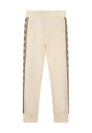 Pantalons de survêtement couleur crème avec taille élastique, présentant des bandes de logo noires sur les côtés et des poignets côtelés. Fabriqués en tissu doux et lisse.