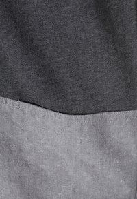 Tessuto grigio scuro con finitura testurizzata nella parte superiore, che sfuma in un materiale grigio chiaro e liscio nella parte inferiore; dettaglio della cucitura visibile.